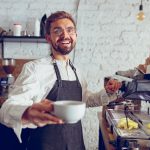 Cheerful male barista offering coffee in cafe