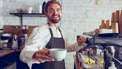 Cheerful male barista offering coffee in cafe